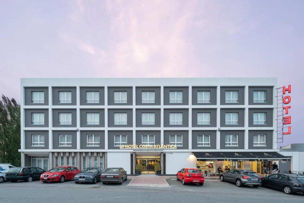 un grand bâtiment avec des voitures garées dans un parking dans l'établissement Hotel Costa Atlántica, à Arteixo