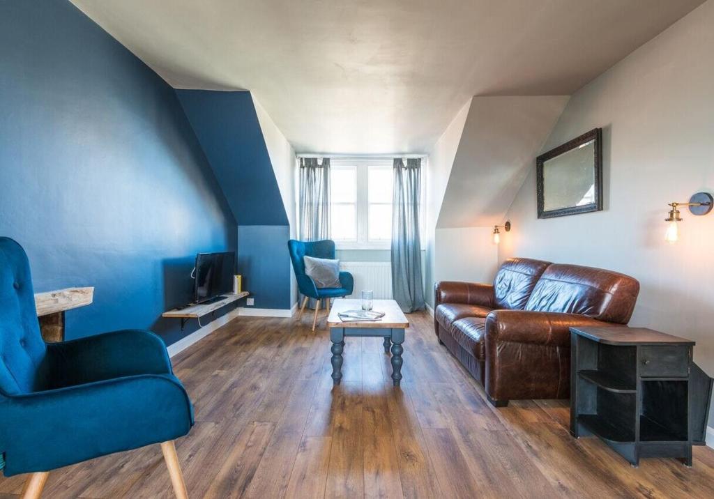 sala de estar con sofá de cuero marrón y sillas azules en SeaView Loft, en Dunbar