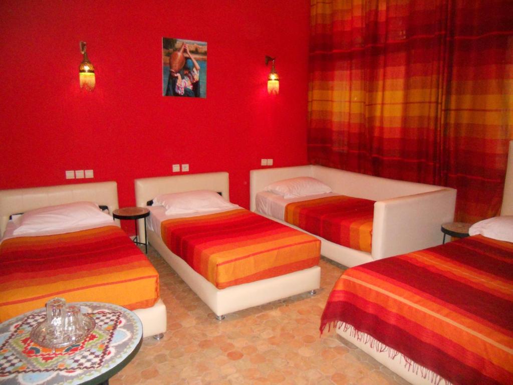 Habitación roja con 3 camas y mesa en Riad Passiflora en Fez