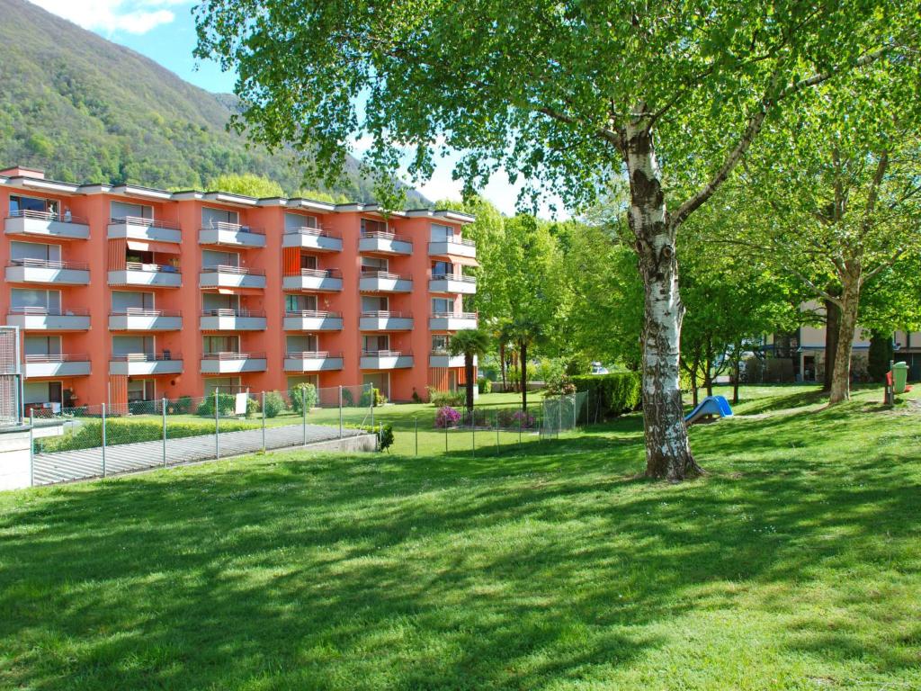 un immeuble d'appartements orange dans un parc avec un arbre dans l'établissement Apartment dei Patrizi, à Losone