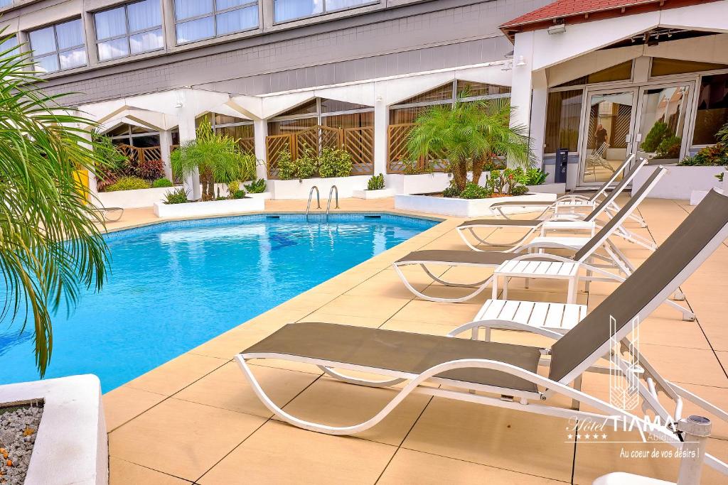 a pool with chaise lounge chairs in front of a building at Hotel Tiama Abidjan in Abidjan