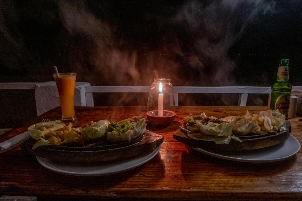 two dishes of food on a wooden table with a candle at Jardim a Mar in Agonda