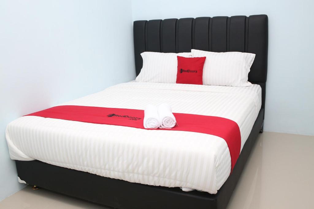 Cama grande con sábanas y almohadas rojas y blancas en RedDoorz Syariah near Suncity Mall Madiun, en Madiun