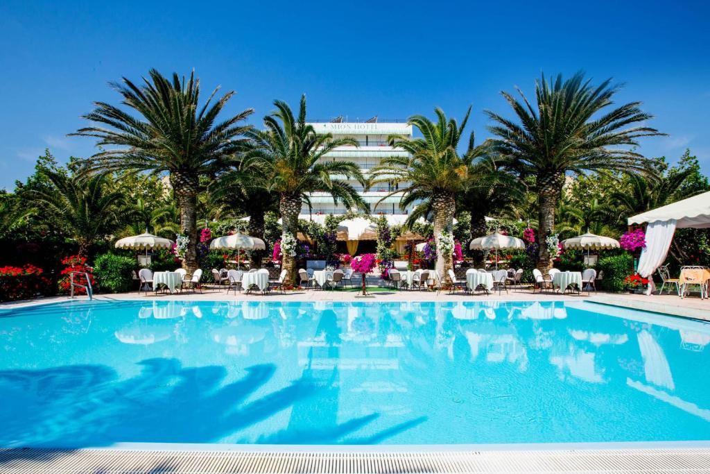 une grande piscine bordée de palmiers et un bâtiment dans l'établissement Hotel Mion Charme & Relax, à Silvi Marina