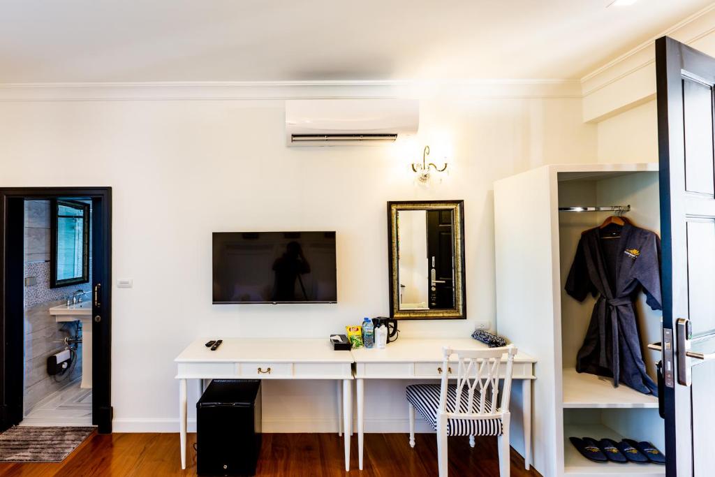 A room workspace with a white desk, mirror, television, mini-fridge and open wardrobe beside the bathroom entrance.