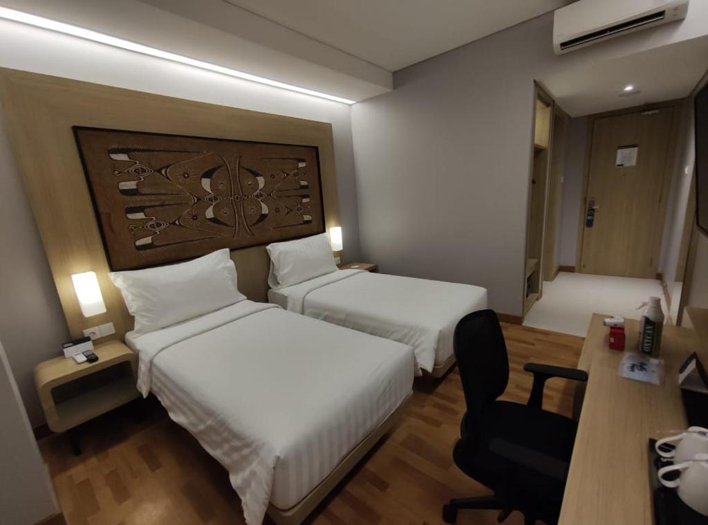 Habitación de hotel con 2 camas, escritorio y silla en BATIQA Hotel Jayapura, en Jayapura
