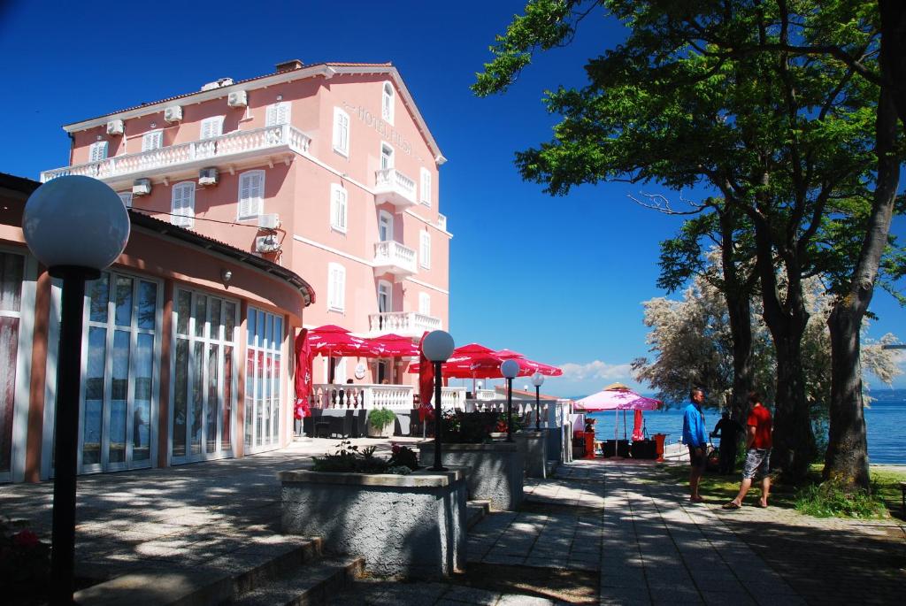 a pink building with red umbrellas next to the water at Hotel Fiesa in Piran