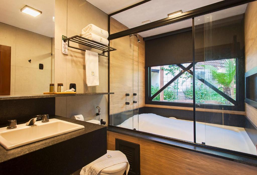 baño con bañera, lavabo y ventana en Hotel Fioreze Chalés en Gramado