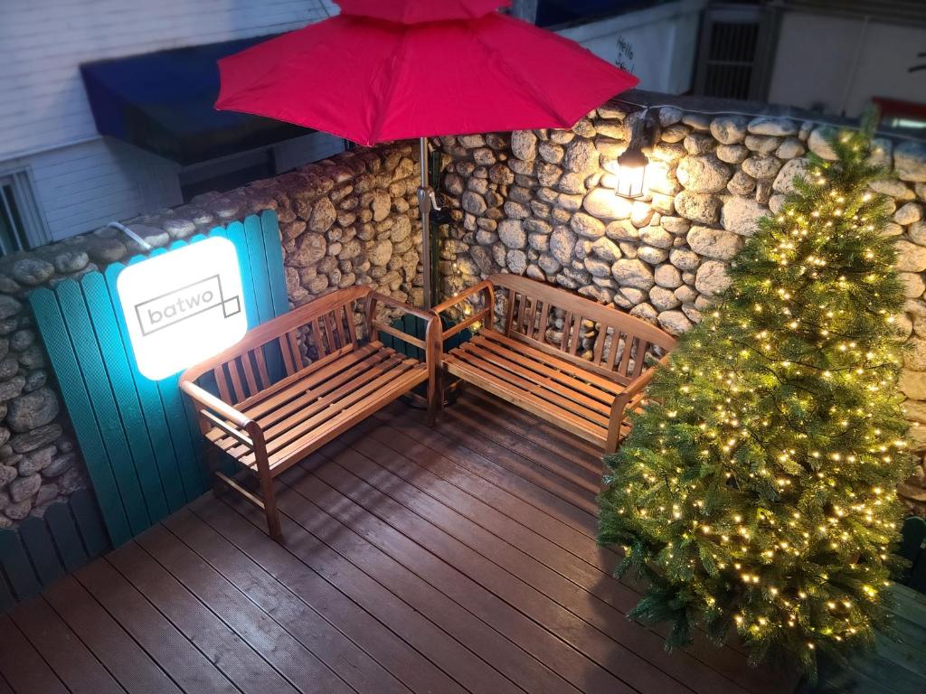 ein Weihnachtsbaum auf einem Deck mit zwei Bänken und einem Regenschirm in der Unterkunft Batwo Stay - For foreigners only in Seoul