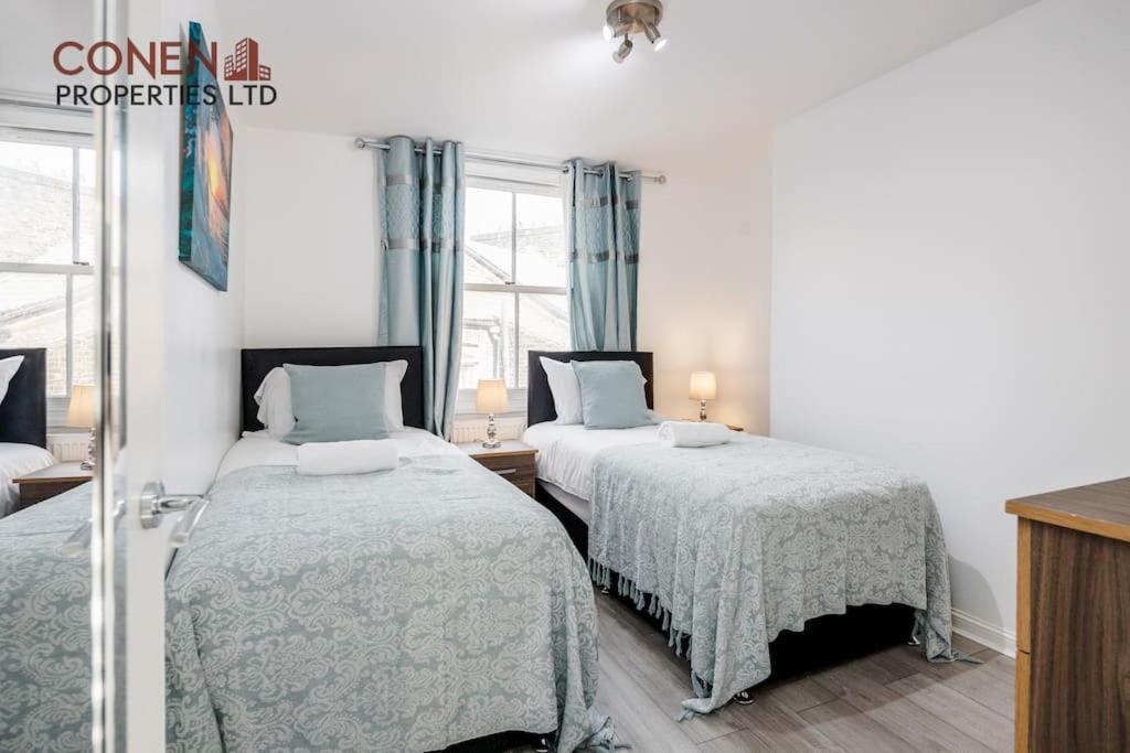 2 Betten in einem weißen Zimmer mit blauen Vorhängen in der Unterkunft CONEN Breccia Apartment in London