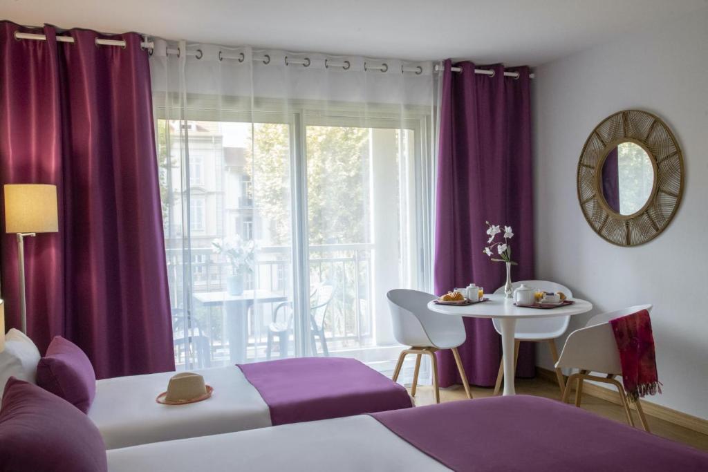 a bedroom with purple curtains and a table and a window at Hotel Chambord in Menton
