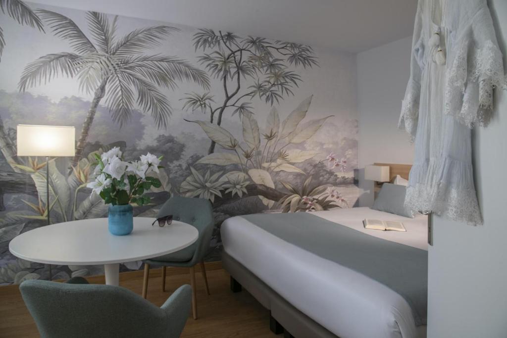 a bedroom with a bed and a table and palm trees wallpaper at Hotel Chambord in Menton