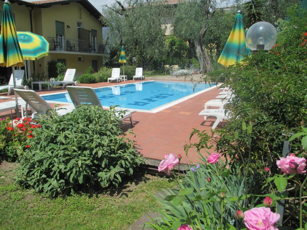 a swimming pool with chairs and umbrellas and flowers at Hotel Casa Popi in Malcesine