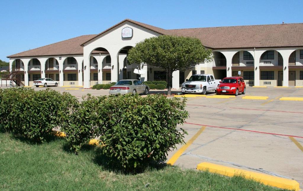 ein Gebäude mit Autos auf einem Parkplatz in der Unterkunft Weatherford Heritage Inn in Weatherford