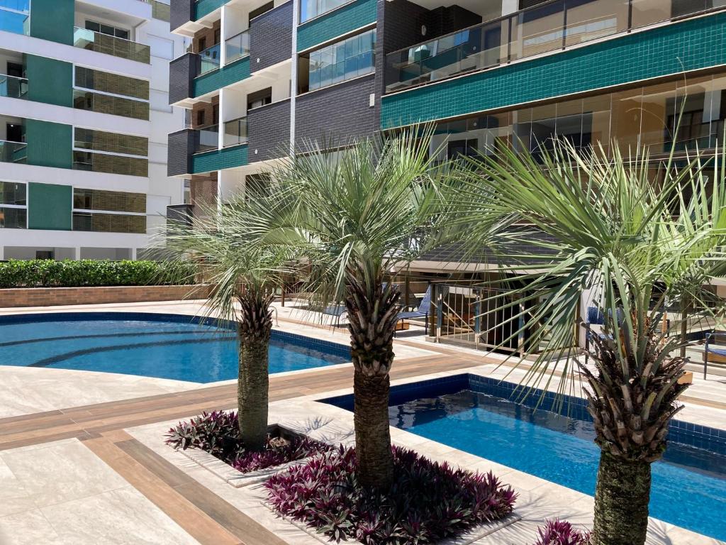 una piscina con 2 palmeras frente a un edificio en Spazio di Patricia, en Governador Celso Ramos