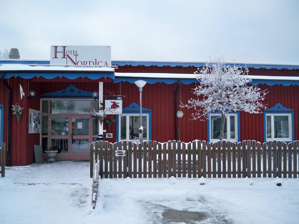 a red building with a fence in the snow at Hotel Nordica Strömsund in Strömsund