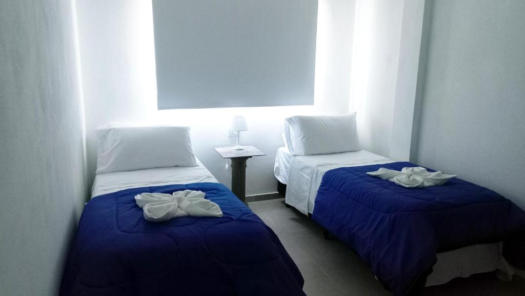 two beds in a room with blue sheets and white pillows at Hotel Musto in Rosario