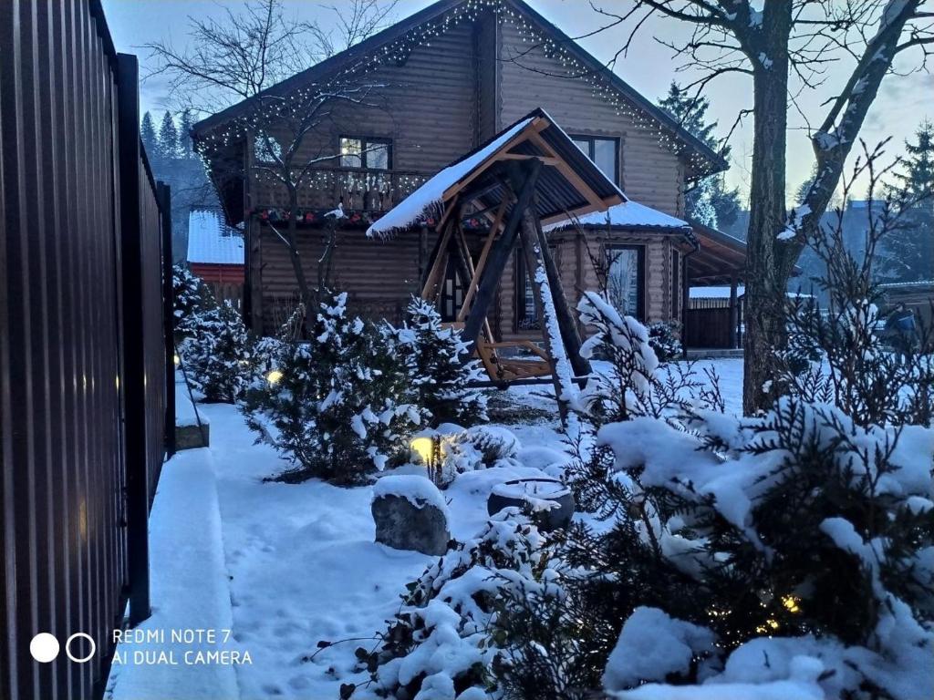 una cabaña de madera en la nieve con luces de Navidad en Берлога 2, en Mykulychyn