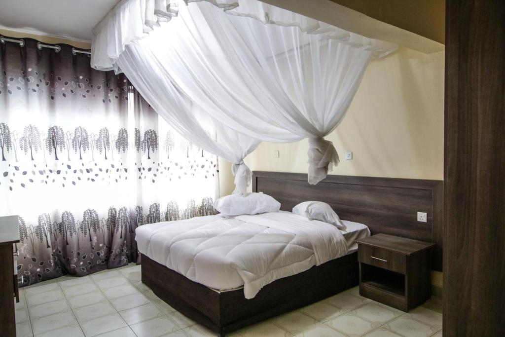 The Siron Place Hotel في Ongata Rongai : غرفة نوم بسرير ابيض مع ستائر ونافذة