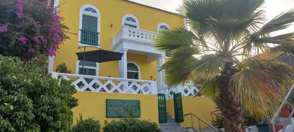 a yellow house with a palm tree in front of it at Hotel Savana in São Filipe