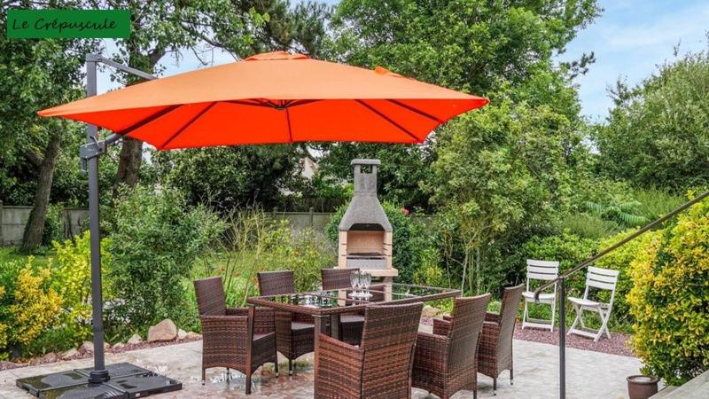 une table et des chaises sous un parasol orange dans l'établissement Le Crépuscule, 300m de la plage, animaux de compagnie bienvenue, à Gouville-sur-Mer