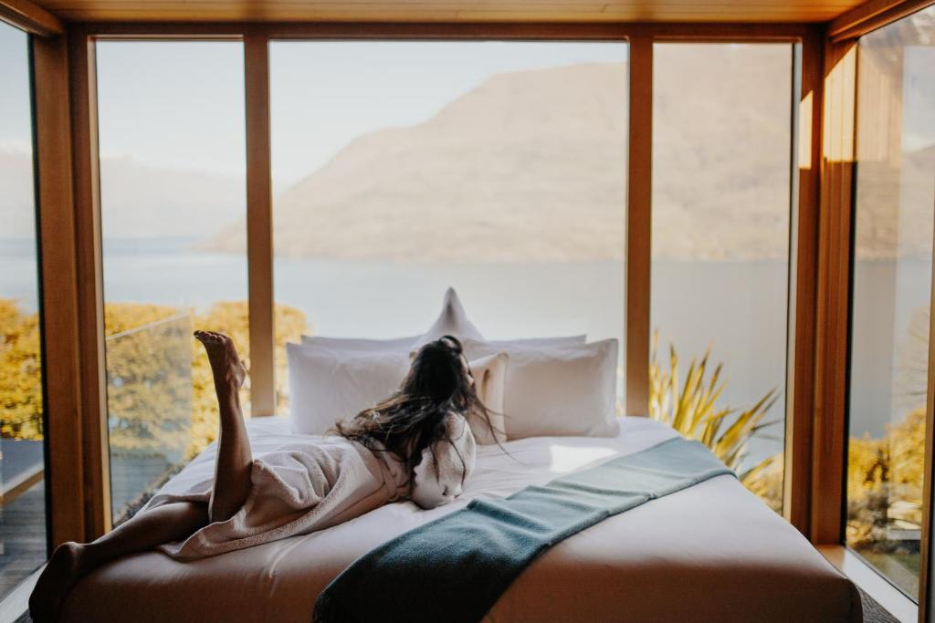 
a woman laying on a bed in front of a window at Azur Lodge in Queenstown
