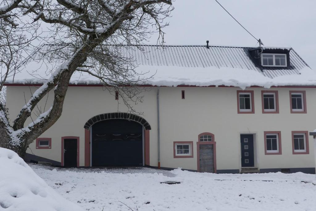 a white building with a black door in the snow at Eifel Bauernhaus Müllesch in Berenbach