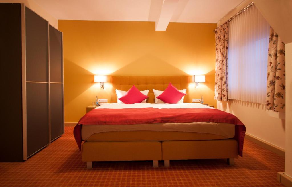 a bedroom with a bed with red sheets and pink pillows at Landgasthof Schneider, Westfeld in Schmallenberg