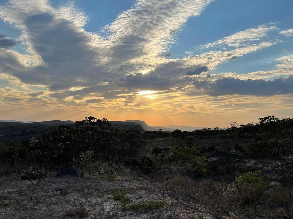 a sunset in a field with a cloudy sky at Pousada Serra da Paz in Carrancas