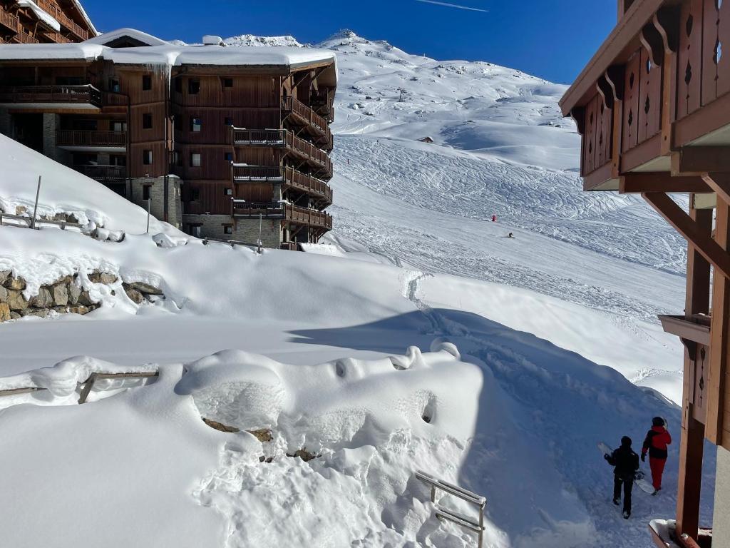 two people walking down a snow covered slope next to a building at Appartement ski aux pieds dans résidence premium piscine, sauna hamam in Les Menuires