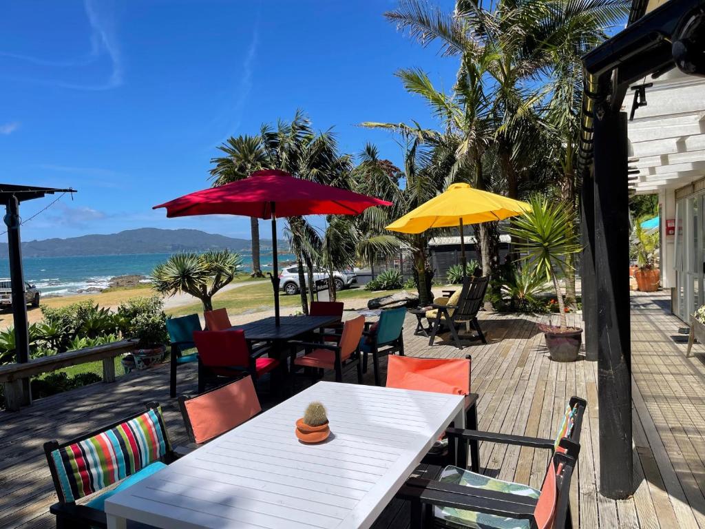 a table and chairs with umbrellas and the beach at Driftwood Beachfront Accommodation, Cable Bay, Owhetu in Coopers Beach
