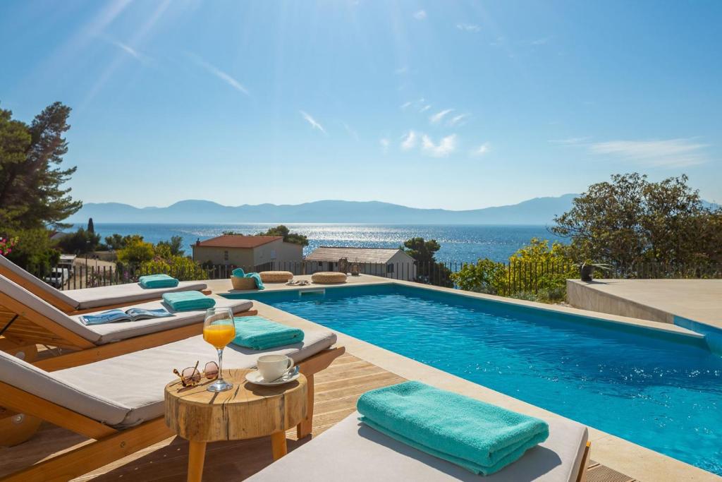 einen Pool mit Stühlen, einem Tisch und einem Glas Wein in der Unterkunft Luxury Villa Azul Makarska with private pool in Podaca