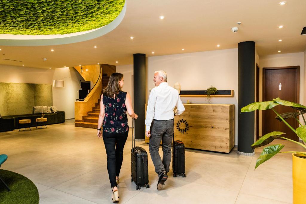 a man and woman walking through a hotel lobby with their luggage at Wirthshof Hotel & Chalets in Markdorf