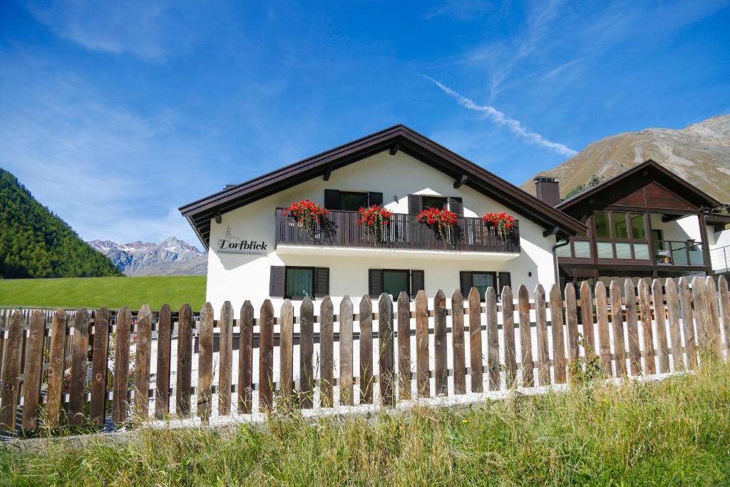 une maison blanche avec une clôture et des fleurs dans l'établissement Dorfblick Appartements & Rooms, à Senales