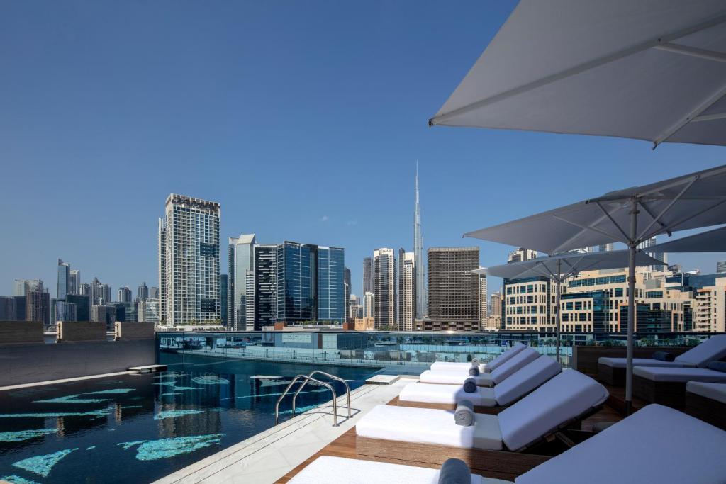 einen Pool mit weißen Liegestühlen und einer Skyline der Stadt in der Unterkunft Hyde Hotel Dubai in Dubai