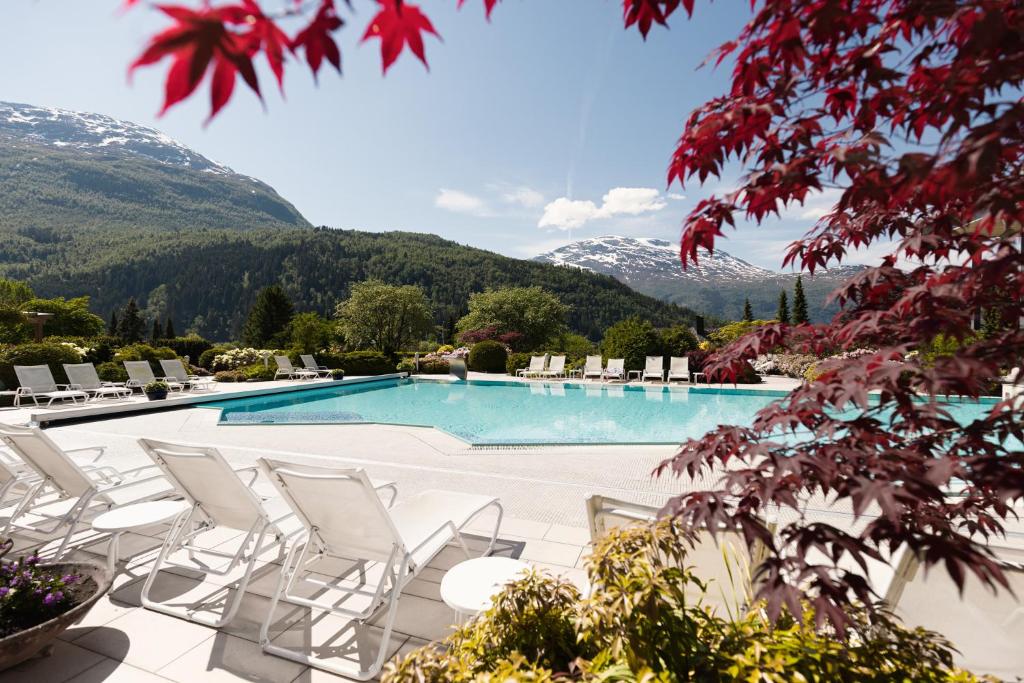 uma piscina com cadeiras e montanhas ao fundo em Hotel Alexandra Loen em Loen