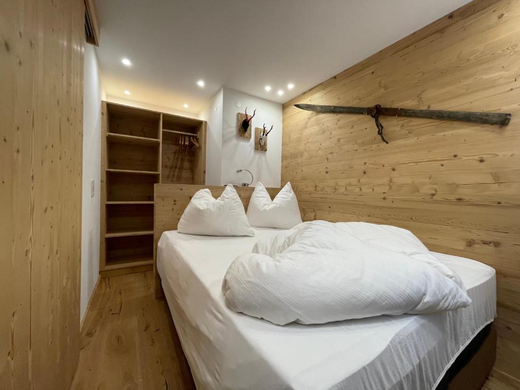 a bedroom with a white bed with a wooden wall at Quality Hosts Arlberg - ALPtyrol Appartements in Sankt Anton am Arlberg