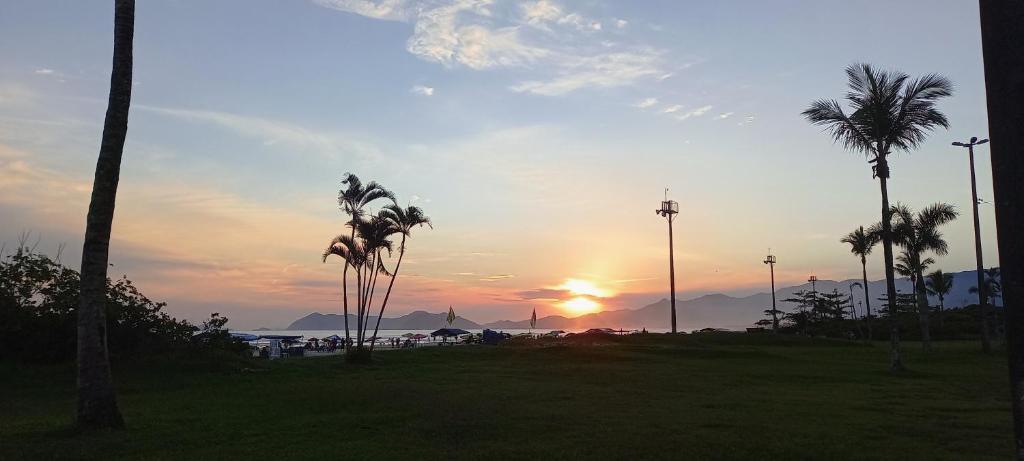 a sunset in a park with palm trees and the sun at Cantinho do Indaiá - Apto pé na areia in Bertioga