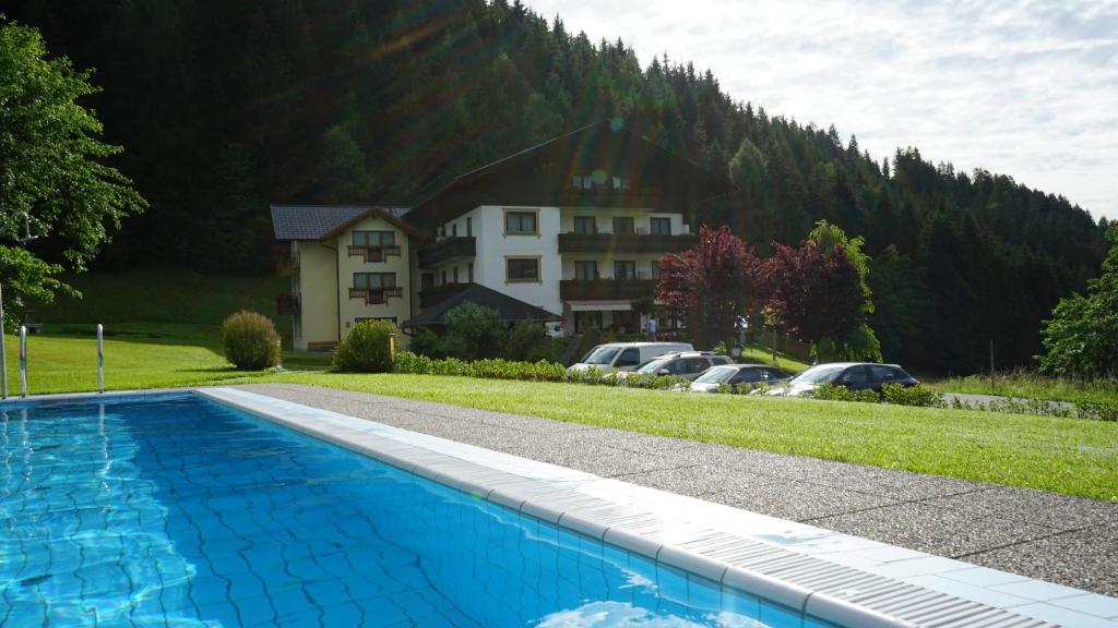 a swimming pool in front of a house with a mountain at Hotel-Pension Birkenhof in Kötschach