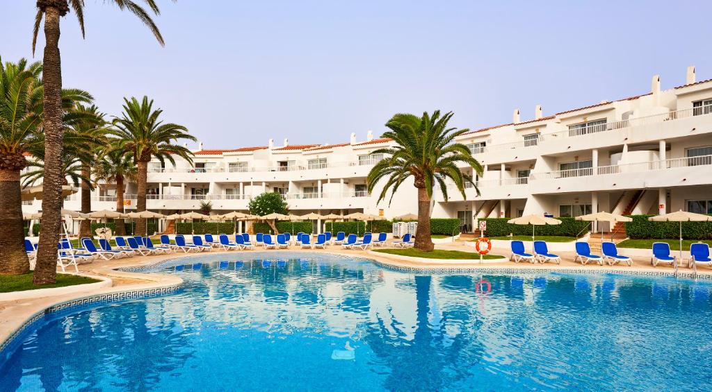 a swimming pool with chairs and palm trees and a hotel at Globales Los Delfines in Cala en Blanes