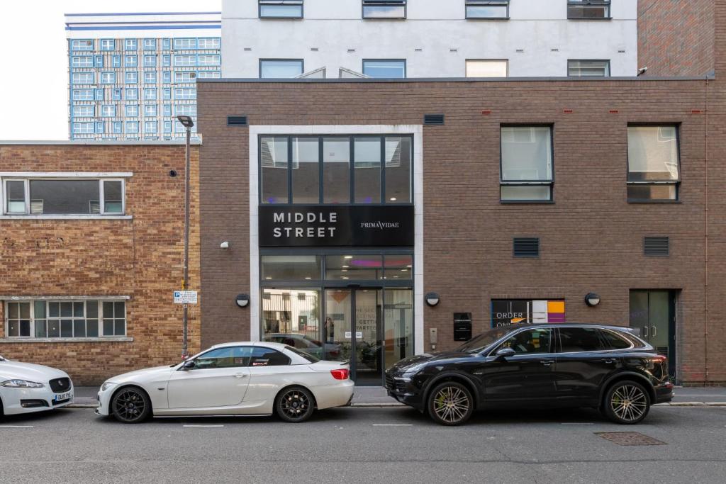 2 voitures garées sur un parking en face d'un immeuble dans l'établissement For Students Only Studios Apartments at Middle Street in Portsmouth City Centre, à Portsmouth