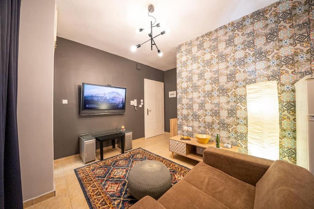 a living room with a couch and a tv on a wall at Kozani Hideaway for 2! in Kozani