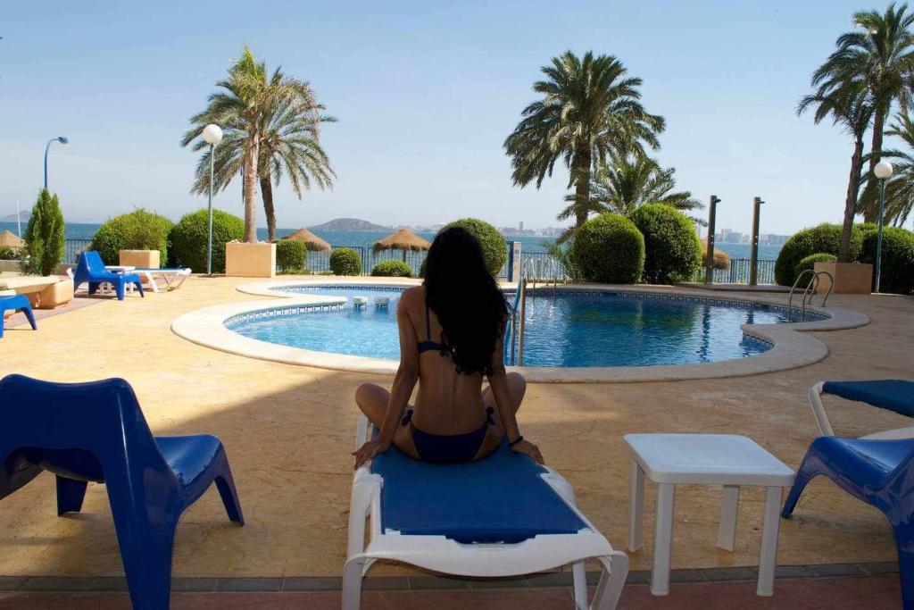 a woman sitting on a chair in front of a swimming pool at ShoreHouse Apartamento Primera linea Playa Honda in Playa Honda