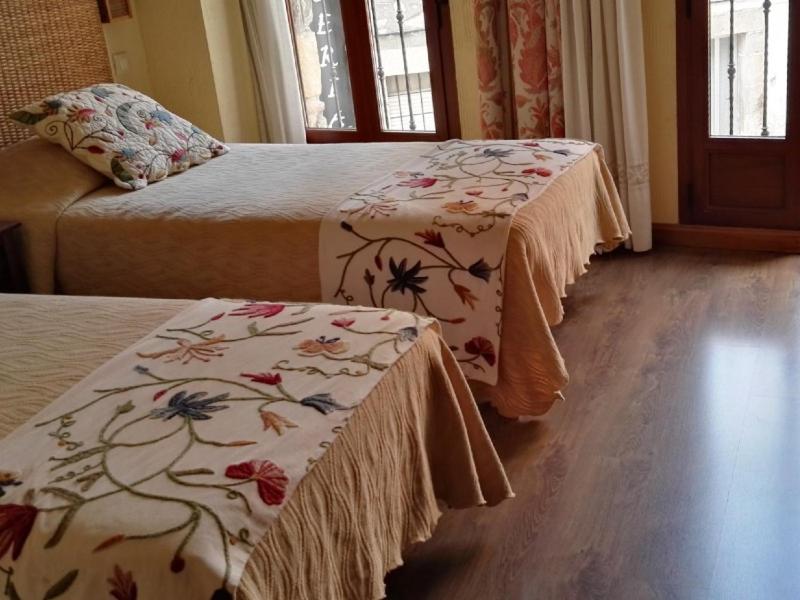 2 Betten in einem Hotelzimmer mit 2 Tischen und Blumen in der Unterkunft Hospedería Tía María in Casillas