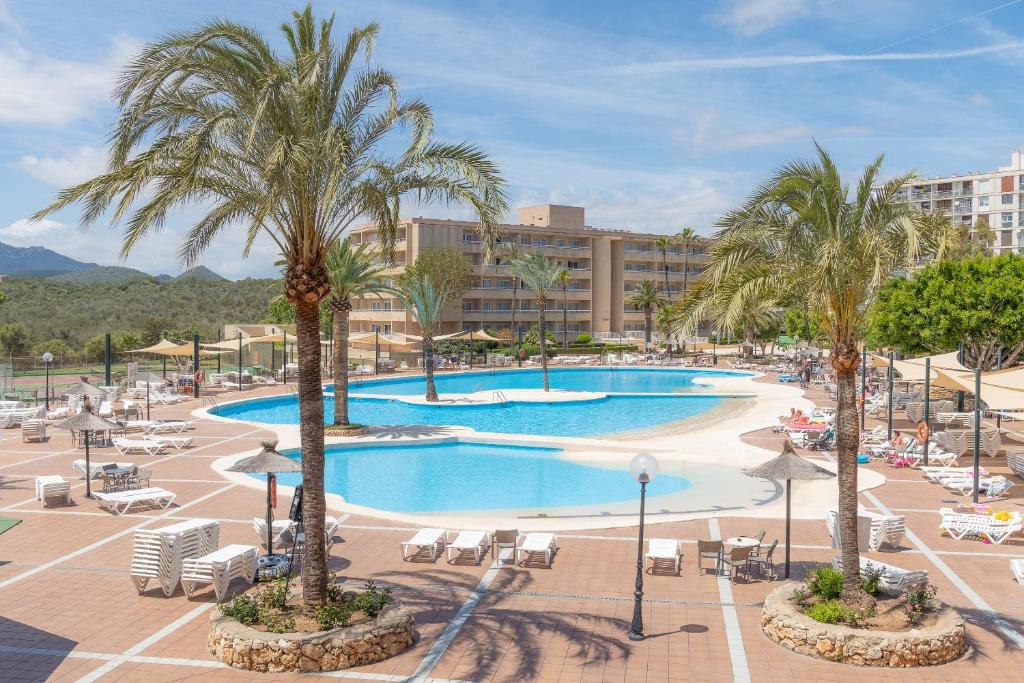 a resort with a pool and palm trees and chairs at Hotel Club Cala Romani in Calas de Mallorca