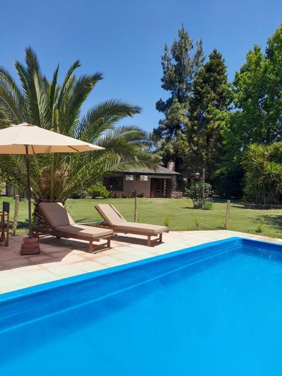 a swimming pool with two lounge chairs and an umbrella at Alto Chacras Cottage in Chacras de Coria
