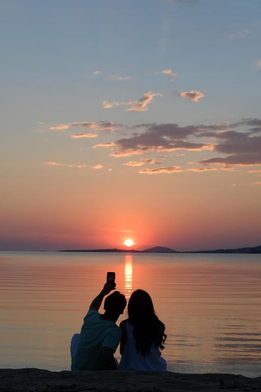 a couple sitting on the beach taking a picture of the sunset at Akti Toroni Boutique Hotel in Toroni