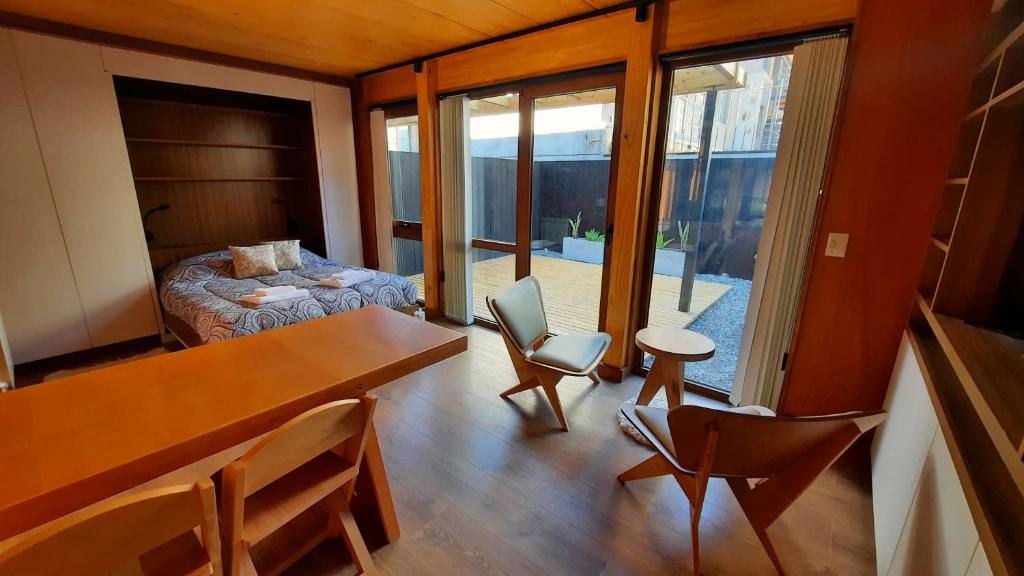 a room with a table and chairs and a bedroom at Hermoso monoambiente con jardin, modernoso y cálido a media cuadra de la calle principal (V406) in San Martín de los Andes