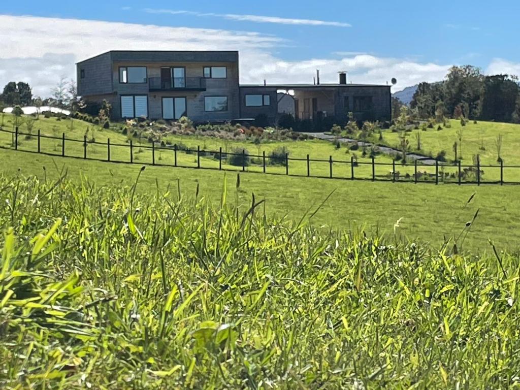 a house on top of a green field with a fence at Cabañas Arrayanes de Huillinco en Chiloé in Chonchi