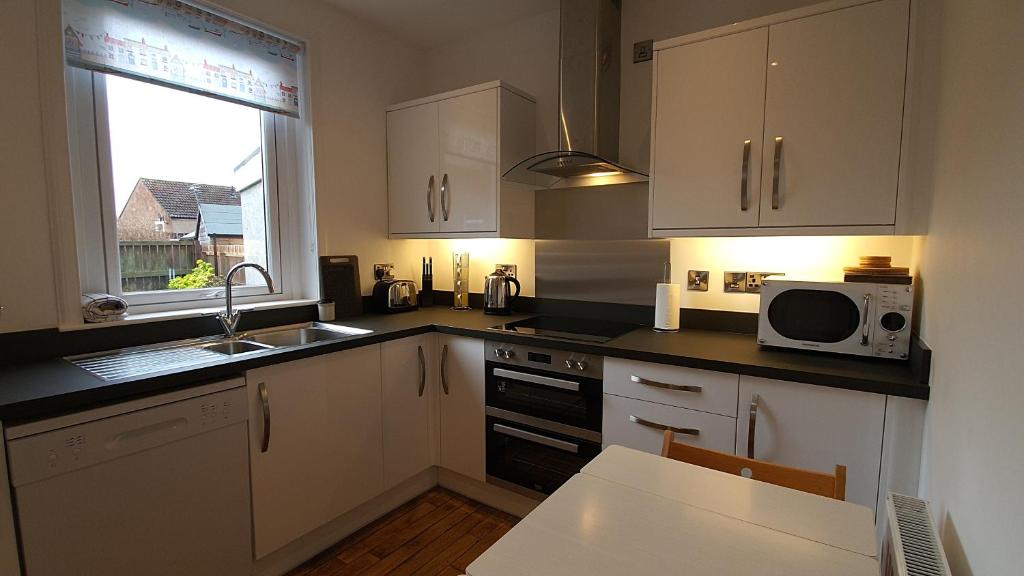 a kitchen with white cabinets and a sink and a microwave at 51 Milton Crescent, Anstruther in Anstruther